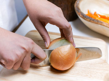 Cropped hands cutting onion on table