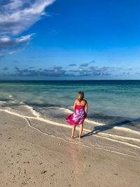 Full length rear view of woman standing on shore at beach against sky
