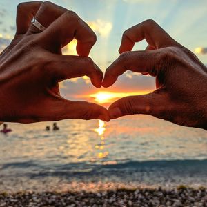 Midsection of heart shape over sea against sky during sunset