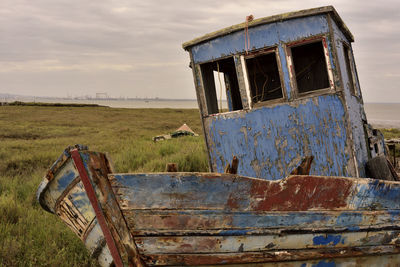 View of obsolete boat by wooden structure on grass with sea in background