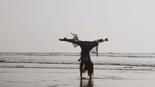 Rear view of woman performing hand stand on shore against sky