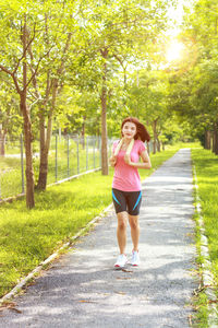 Portrait of woman jogging on footpath against trees