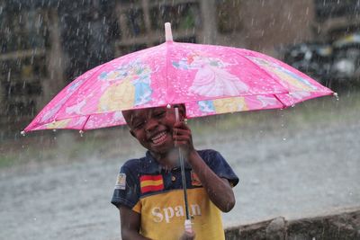 Happy boy holding umbrella during rainy season