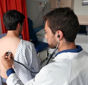 High angle view of doctor checking man with stethoscope in hospital