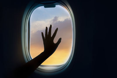 Silhouette hand against sky during sunset seen through airplane window