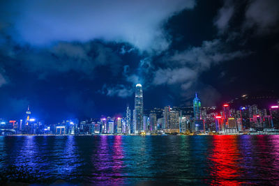 Illuminated city by sea against sky at night