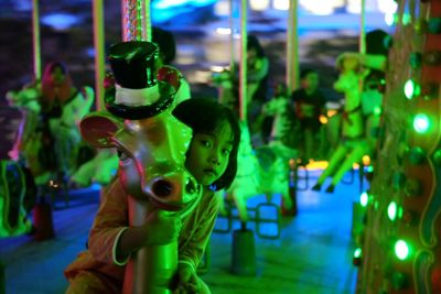 Girl on illuminated carousel in amusement park