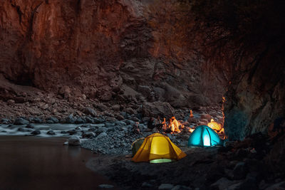 Illuminated tent by rock formation in cave