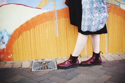 Low section of woman walking on sidewalk by graffiti wall