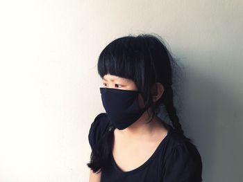 Girl wearing mask looking away while standing against wall