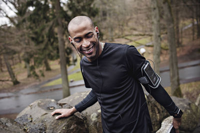 Happy male athlete listening music while exercising by stone wall in forest