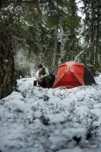 Man in winter forest in front of tent