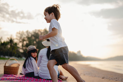 Side view of siblings playing on beach against sky