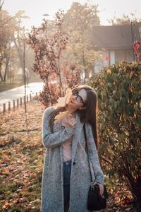 Portrait of young woman standing with autumn leaf by plants