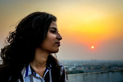 Portrait of young woman looking away against sky during sunset