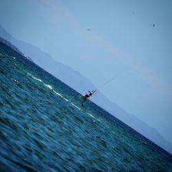 Man fishing in sea against clear blue sky