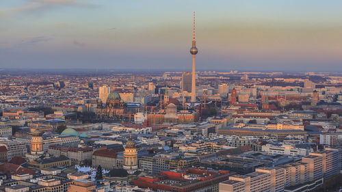 Fernsehturm amidst cityscape against sky during sunset