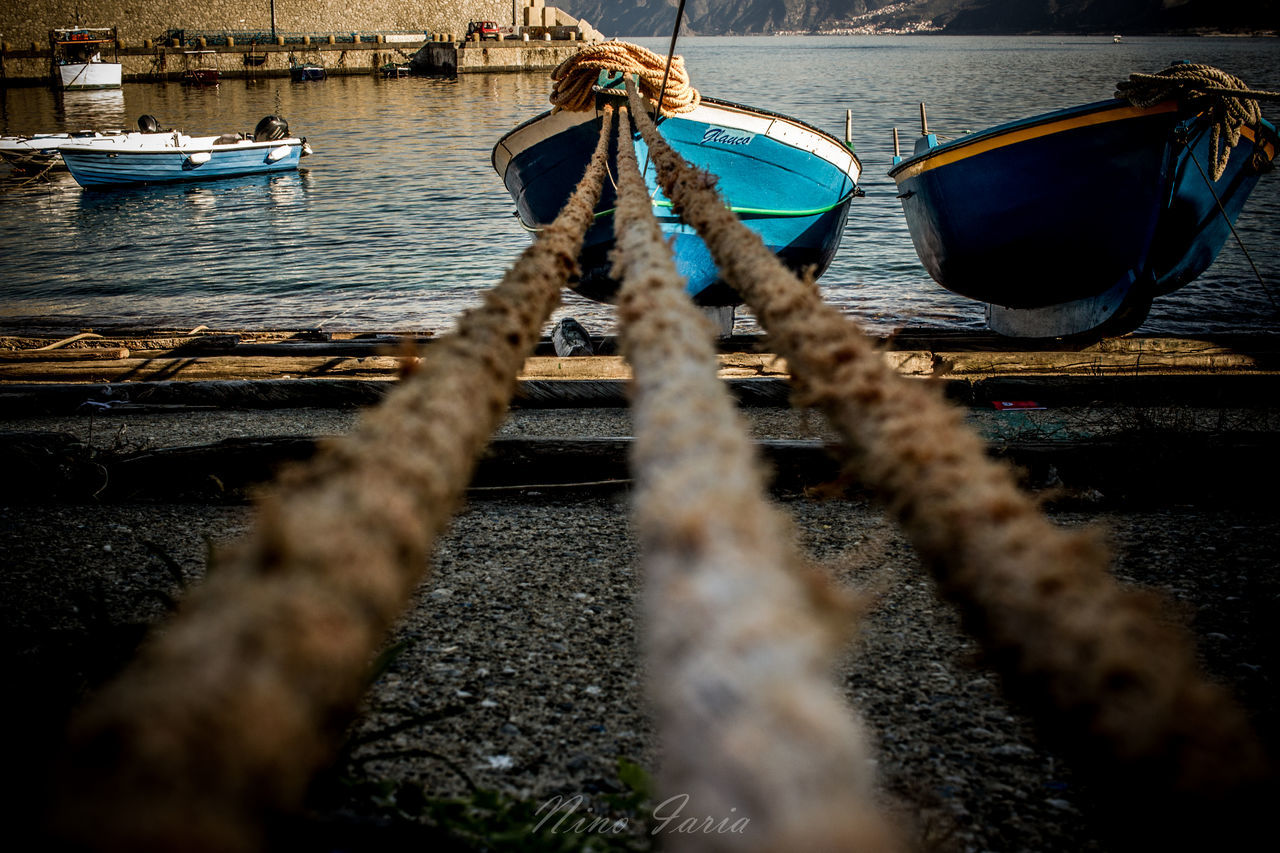 water, nautical vessel, transportation, reflection, mode of transportation, boat, nature, moored, vehicle, sea, blue, day, ship, no people, morning, outdoors, darkness, watercraft, focus on background, rope, travel, selective focus, sunlight, beach