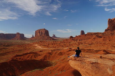Man standing on rock formation in desert against sky