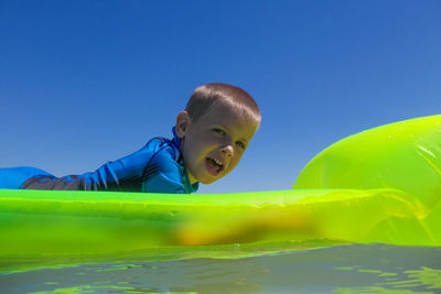 Portrait of boy lying on pool raft in sea against clear sky