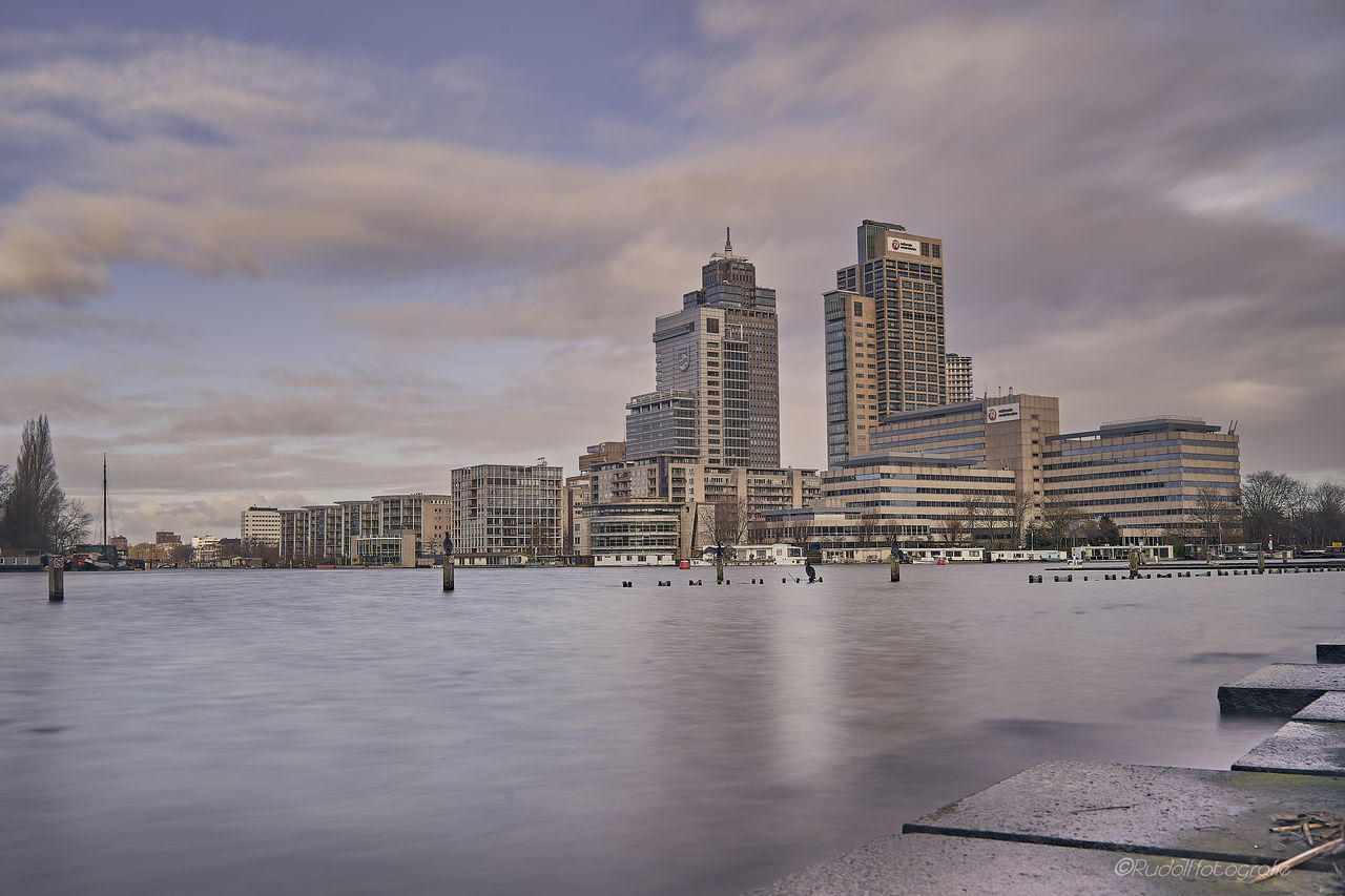 MODERN BUILDING BY RIVER AGAINST SKY