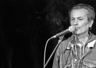 Mature musician by microphone against black background