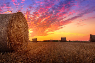 Hay bales on field against sky during sunset