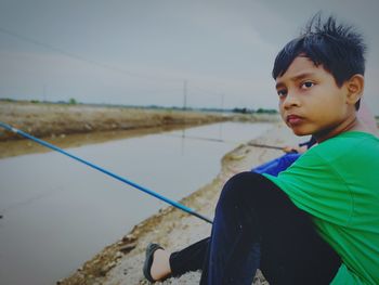 Boy looking away while sitting by canal