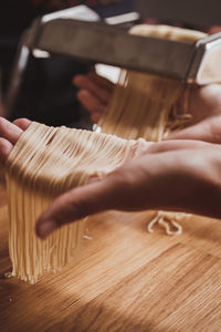 Cropped hand of woman preparing pasta with machine in kitchen