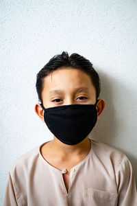 Portrait of young man covering face against white wall