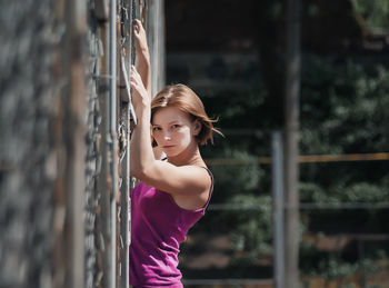 Young sports woman is standing near a metal net on the sports field