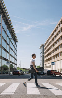 Side view of man with artificial leg carrying skateboard and walking on crosswalk on sunny day on city street