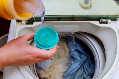 Cropped image of person pouring water in container above washing machine