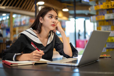 Young woman using mobile phone while sitting on table