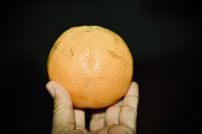 Close-up of hand holding orange against black background