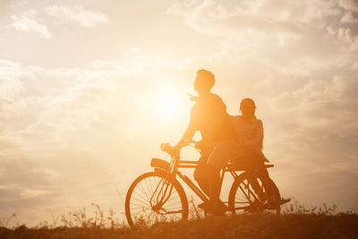 People riding bicycle against sky during sunset