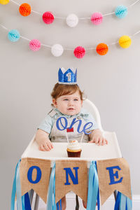 Cute baby boy with cupcake sitting on high chair