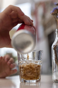 Human hand pours chilled soft drink into glass with ice cubes