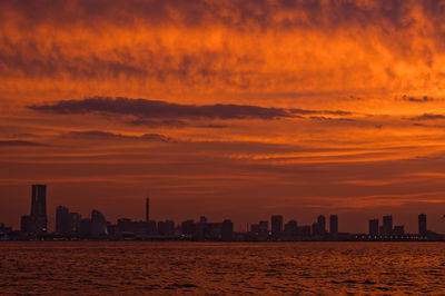 Sea by buildings against sky during sunset