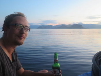 Portrait of smiling man drinking beer while sitting in boat at sea