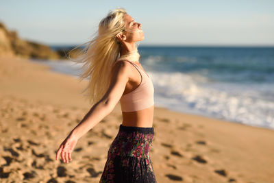 Side view of woman with arms outstretched standing on shore at beach during sunny day