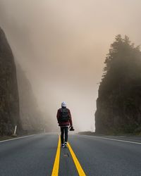 Rear view of man walking on road during foggy weather