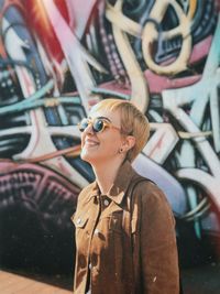 Smiling young woman standing against graffiti wall
