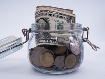 Close-up of coins in jar against white background
