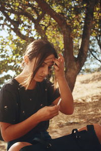 Young woman holding cigarette while sitting on tree