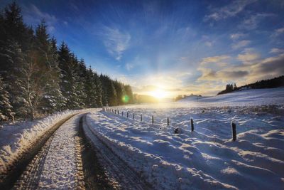 Snow covered field against sky during sunset