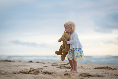 Girl with stuffed toy at beach against sky