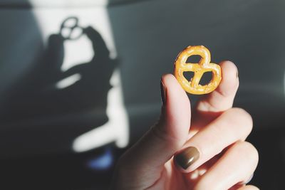 Cropped hand of woman holding pretzel against wall