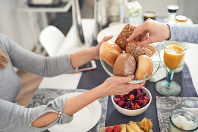 Cropped hand picking bread from bowl offered by friend