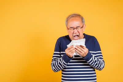 Portrait of young man holding box against yellow background